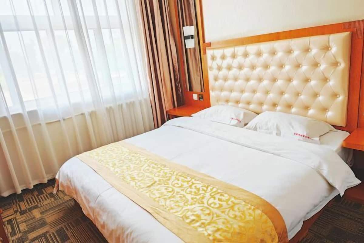 Een hotelkamer met een groot bed, een houten hoofdbord en een raam met gordijnen.