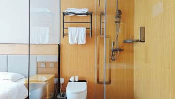 A modern bathroom with a glass shower enclosure, a wooden vanity, and a bed with a white headboard.
