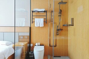 A modern bathroom with a glass shower enclosure, a wooden vanity, and a bed with a white headboard.