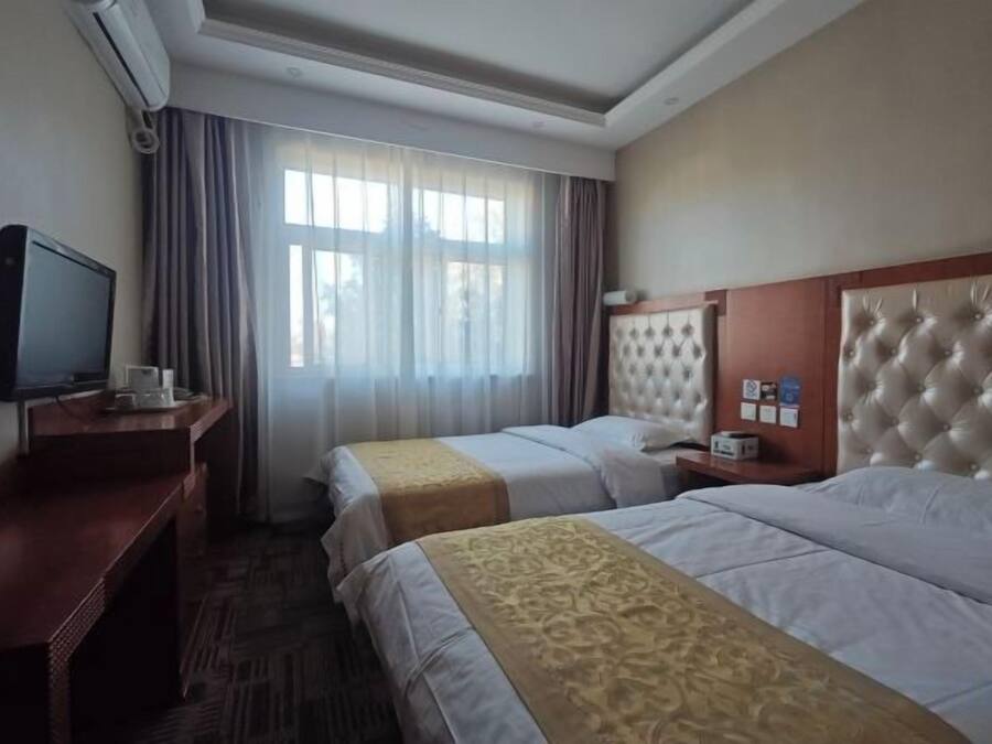 A hotel room with two beds, a television, a desk, and a window with curtains.