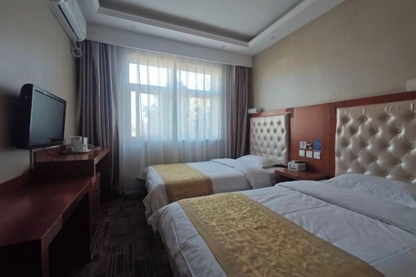 A hotel room with two beds, a television, a desk, and a window with curtains.
