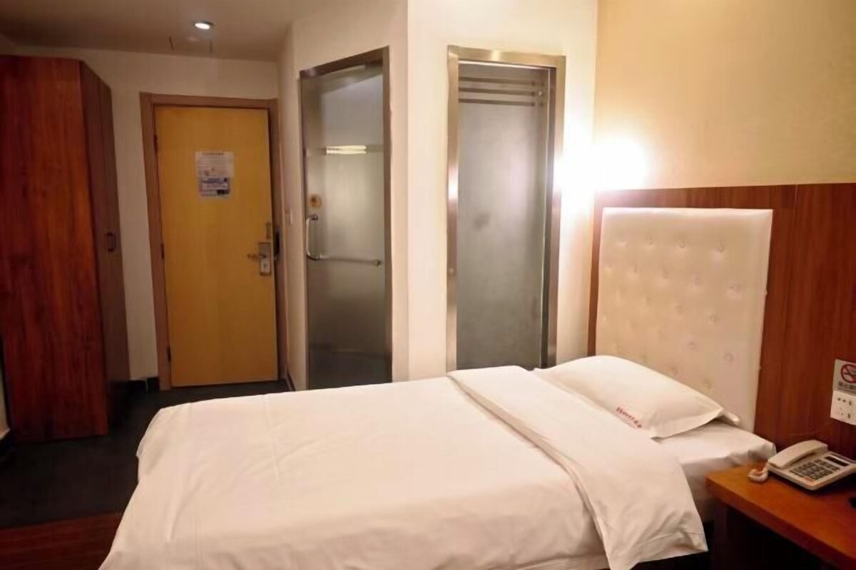 Una habitación de hotel con una cama, un armario de madera, una puerta y un teléfono fijo en la pared.