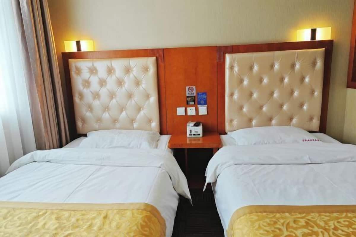 Een hotelkamer met twee bedden, een houten hoofdeinde, een nachtkastje en een wandlamp.