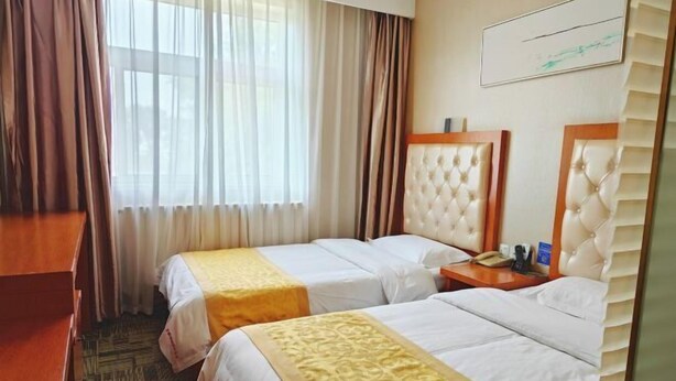 A hotel room with two beds, a desk, a chair, a window with curtains, and a mirror.