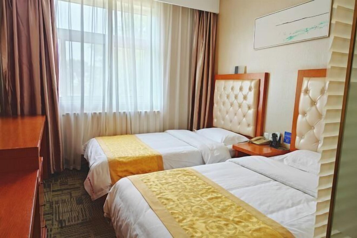 A hotel room with two beds, a desk, a chair, a window with curtains, and a mirror.