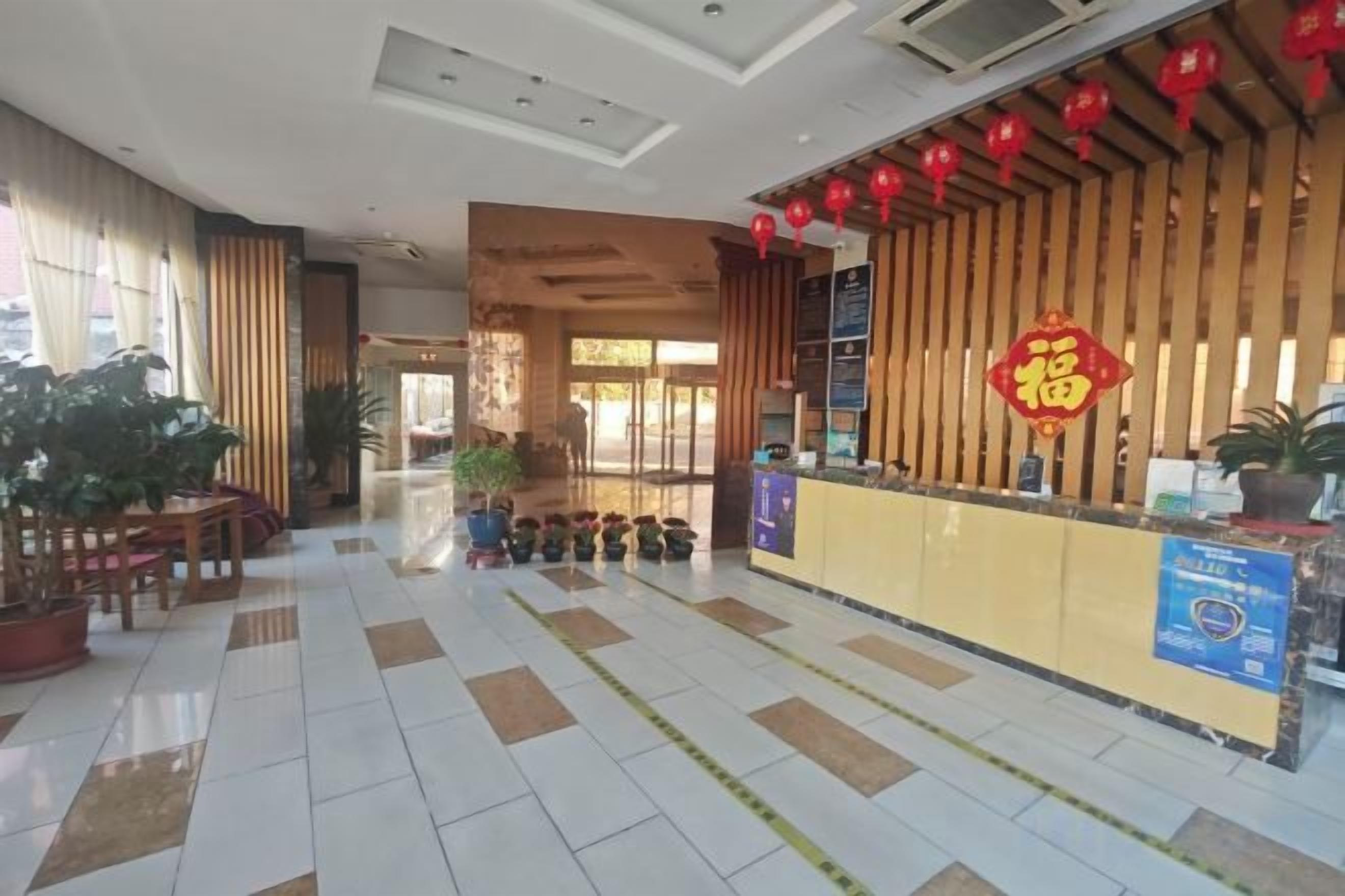 Un vestíbulo de hotel con una mesa de recepción, plantas en macetas y un piso de baldosas.