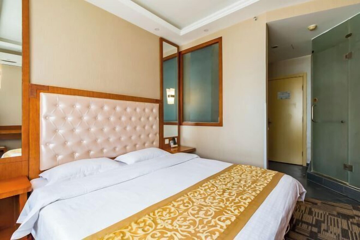 Habitación de hotel con cabecera capitonada, un espejo grande, cama con ropa blanca y un corredor estampado.
