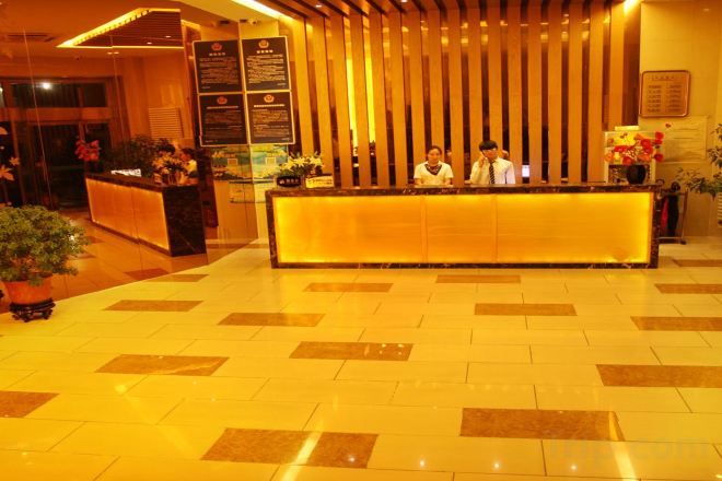 A hotel reception area with a reception desk, a vertical wooden panel, and a tiled floor.