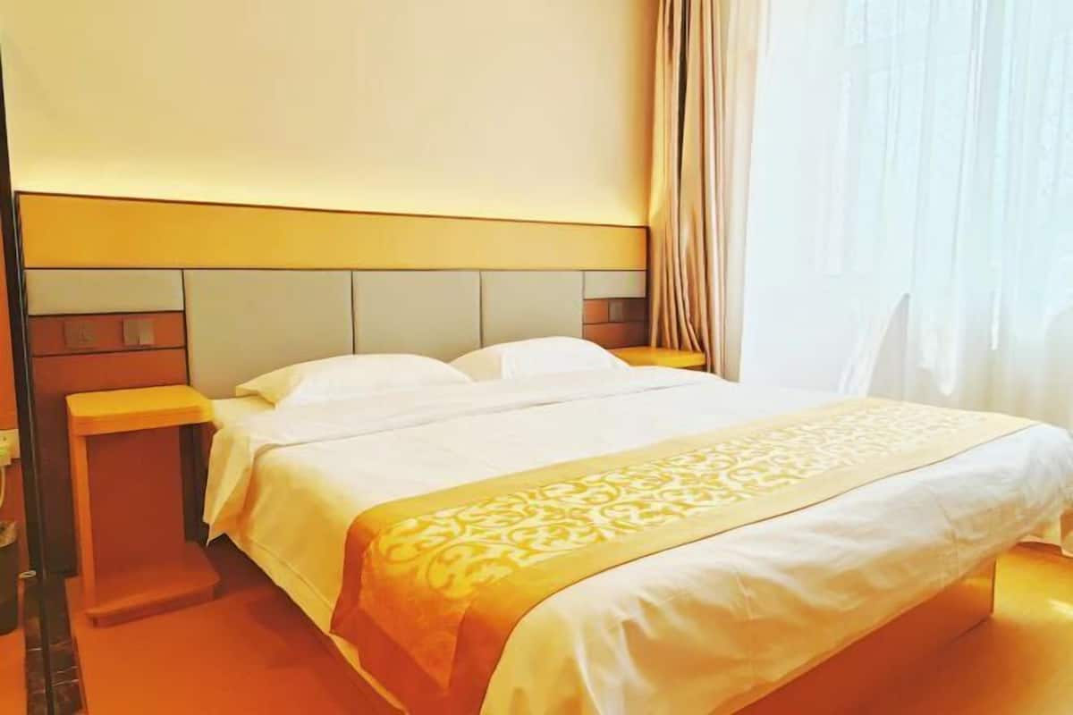 Een hotelkamer met een bed, nachtkastje en een raam met gordijnen.