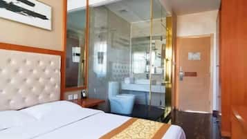A hotel room with a bed, a glass-enclosed shower, a bathroom with a mirror, and a door.