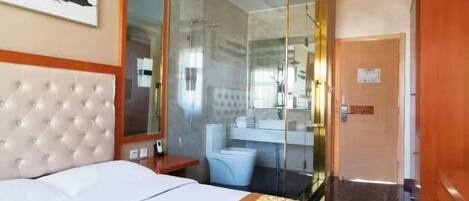 A hotel room with a bed, a glass-enclosed shower, a bathroom with a mirror, and a door.