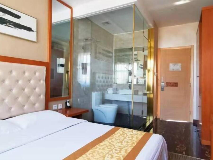 A hotel room with a bed, a glass-enclosed shower, a bathroom with a mirror, and a door.