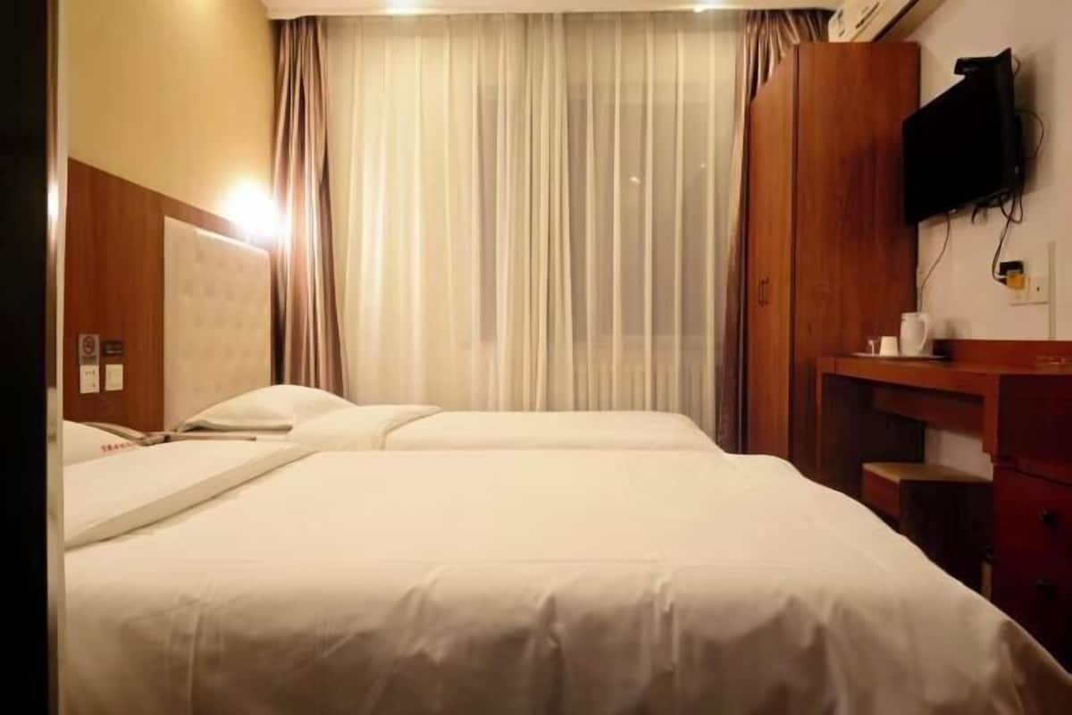 Een hotelkamer met een bed, een bureau, een aan de muur bevestigde televisie en een raam met gordijnen.