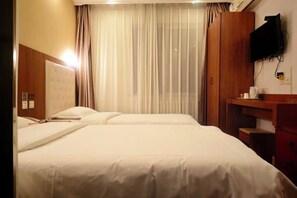 A hotel room with a bed, a desk, a television mounted on the wall, and a window with curtains.
