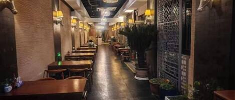 A restaurant with a long counter, wooden tables, and chairs, and wall-mounted lamps.
