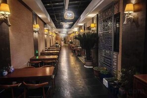 Un restaurante con una barra larga, mesas y sillas de madera, y lámparas fijadas a la pared.