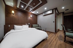 Habitación de hotel con una cama grande, un escritorio con silla, una mesita y aire acondicionado de pared.