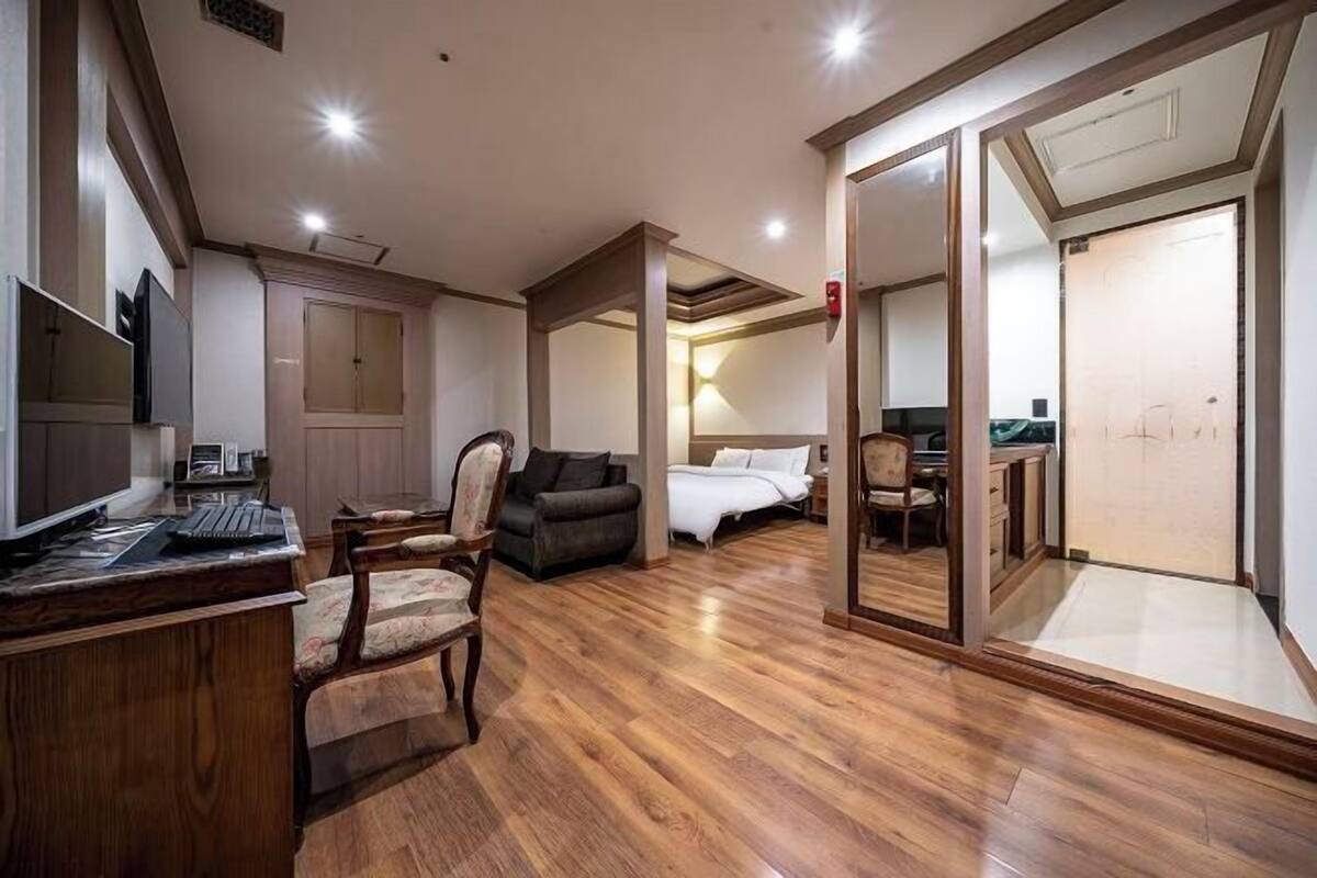 Une chambre d’hôtel avec un plancher en bois, un bureau avec un ordinateur, un canapé, un lit et un grand miroir.