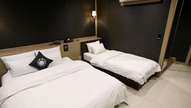Une chambre d’hôtel avec deux lits simples, un mur de couleur sombre et un plancher de couleur claire.