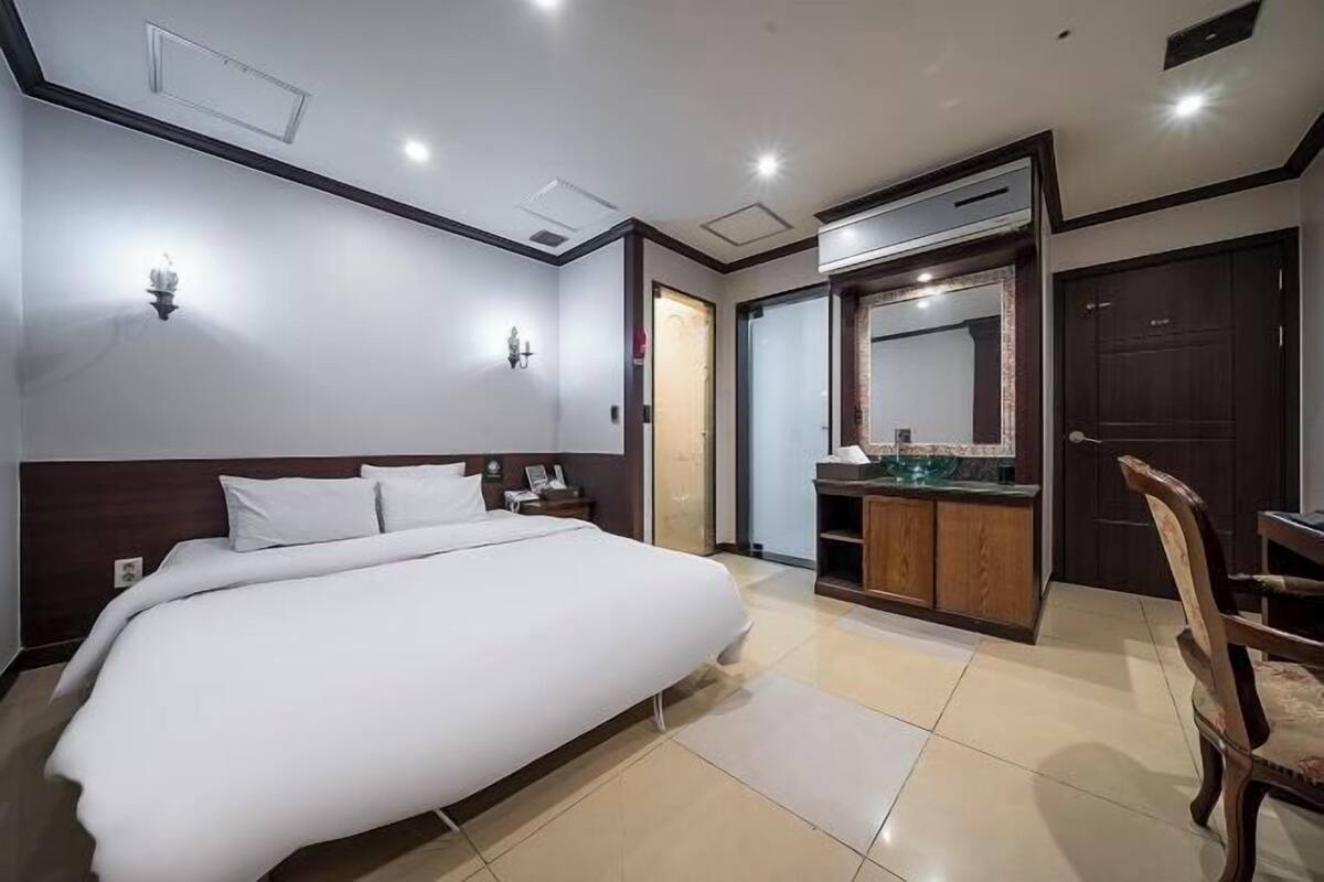 Une chambre d’hôtel avec un grand lit, un bureau avec un miroir et une petite kitchenette.