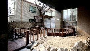 A covered outdoor area with a wooden deck, a small wooden structure, and a view of a house in the background. - Hotel Cullinan Yongin (Yongin-si)