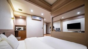 Habitación de hotel con cama, televisión, microondas y pequeña cocina.