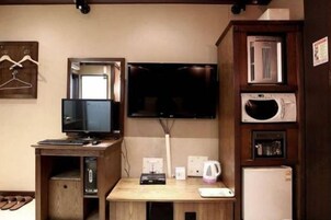 Una habitación con escritorio de madera, televisor montado en la pared, microondas y refrigerador.