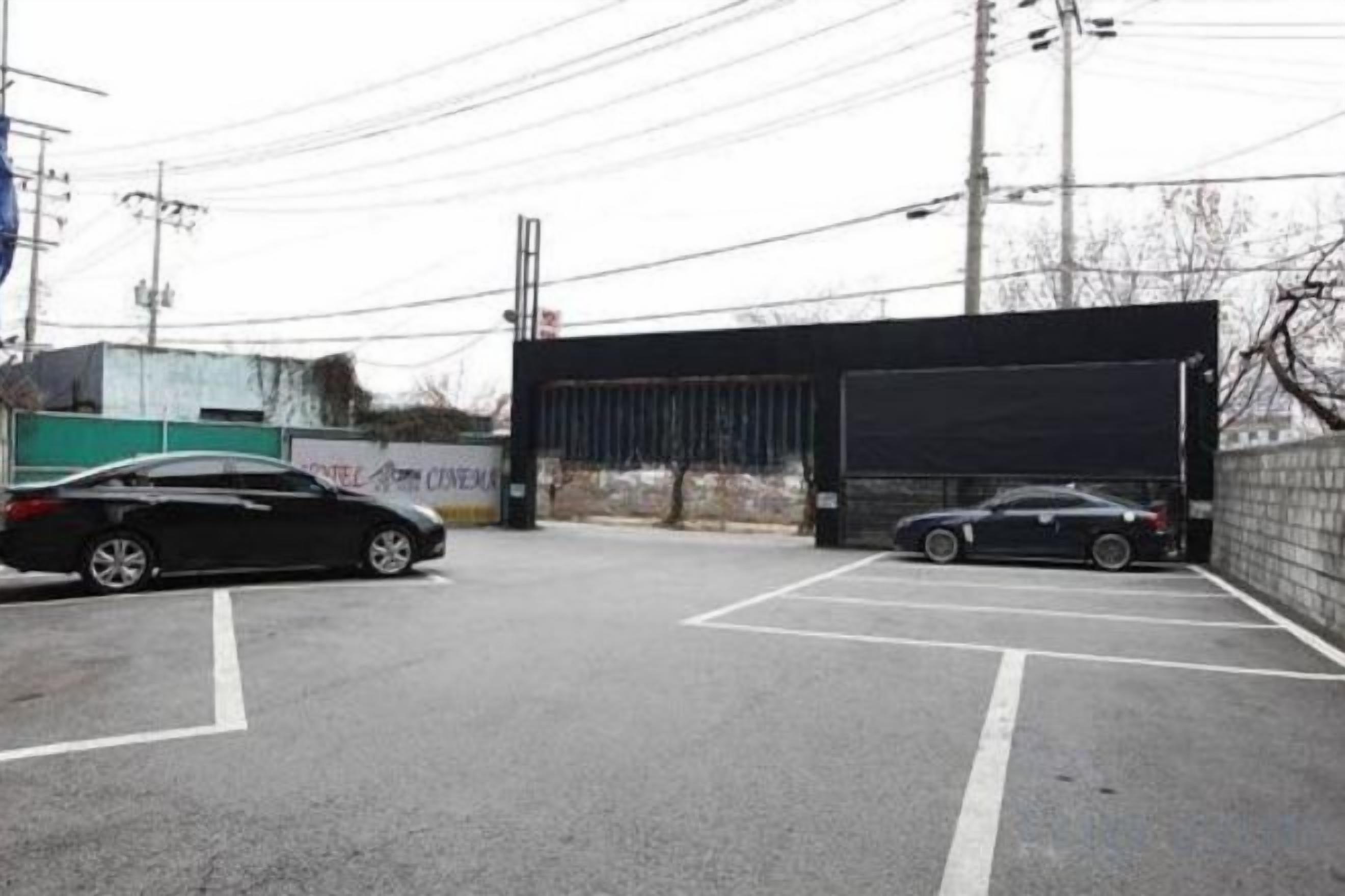 A parking lot with two cars, a building entrance, and a fence.