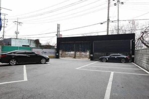 A parking lot with two cars, a building entrance, and a fence. - Hotel Cullinan Yongin (Yongin-si)