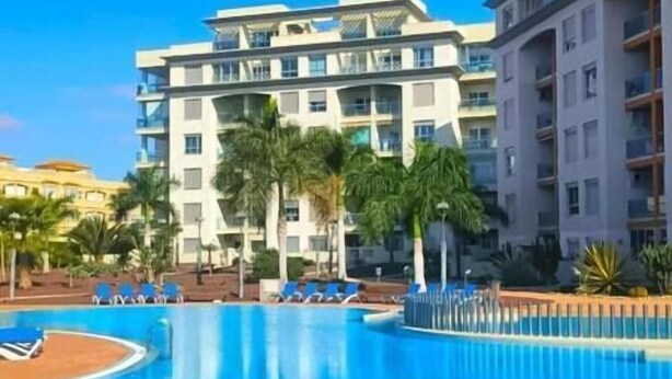 A hotel with a swimming pool, palm trees, and multiple balconies. - Almogrote Sunset South (San Miguel de Abona)