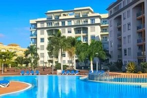Un hôtel doté d’une piscine, de palmiers et de nombreux balcons.