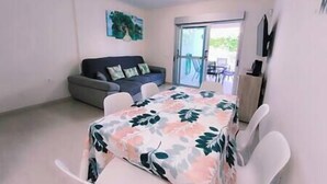 A room with a sofa, a table with chairs, a TV, and a sliding glass door leading to an outdoor area. - Almogrote Sunset South (San Miguel de Abona)