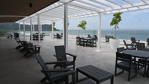 An outdoor seating area with tables and chairs, a covered section, and a view of the ocean. - Jacó beachfront condo in center of town (Jaco)