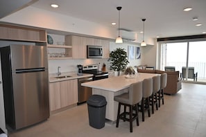 A modern kitchen with a stainless steel refrigerator, microwave, and stove. There is a dining area with a bar stool and a large window.