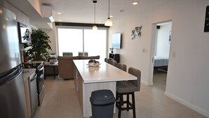 A modern kitchen with a central island, dining area, and a trash bin. - Jacó beachfront condo in center of town (Jaco)