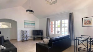 A spacious living room with a black sofa, a flat-screen TV, and a dining area with chairs. - Villa Alicia, Moderne Exklusive Villa in Puerto del Carmen (Tías)