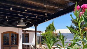 A covered outdoor area with a pool, tables, and chairs, surrounded by greenery and a clear sky. - Villa Alicia, Moderne Exklusive Villa in Puerto del Carmen (Tías)