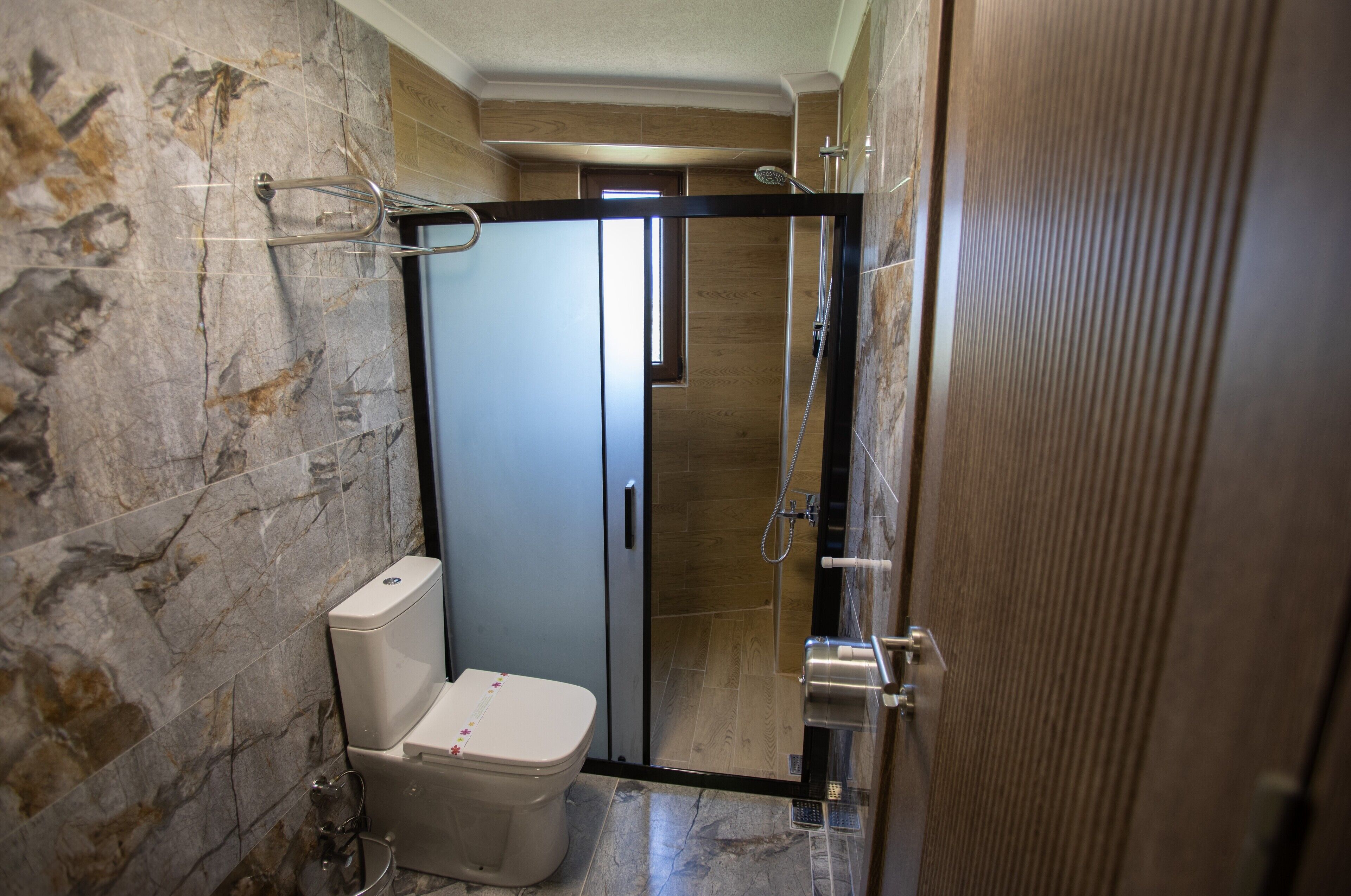Une salle de bain avec un mur en marbre, des toilettes, un espace douche et une porte en bois.
