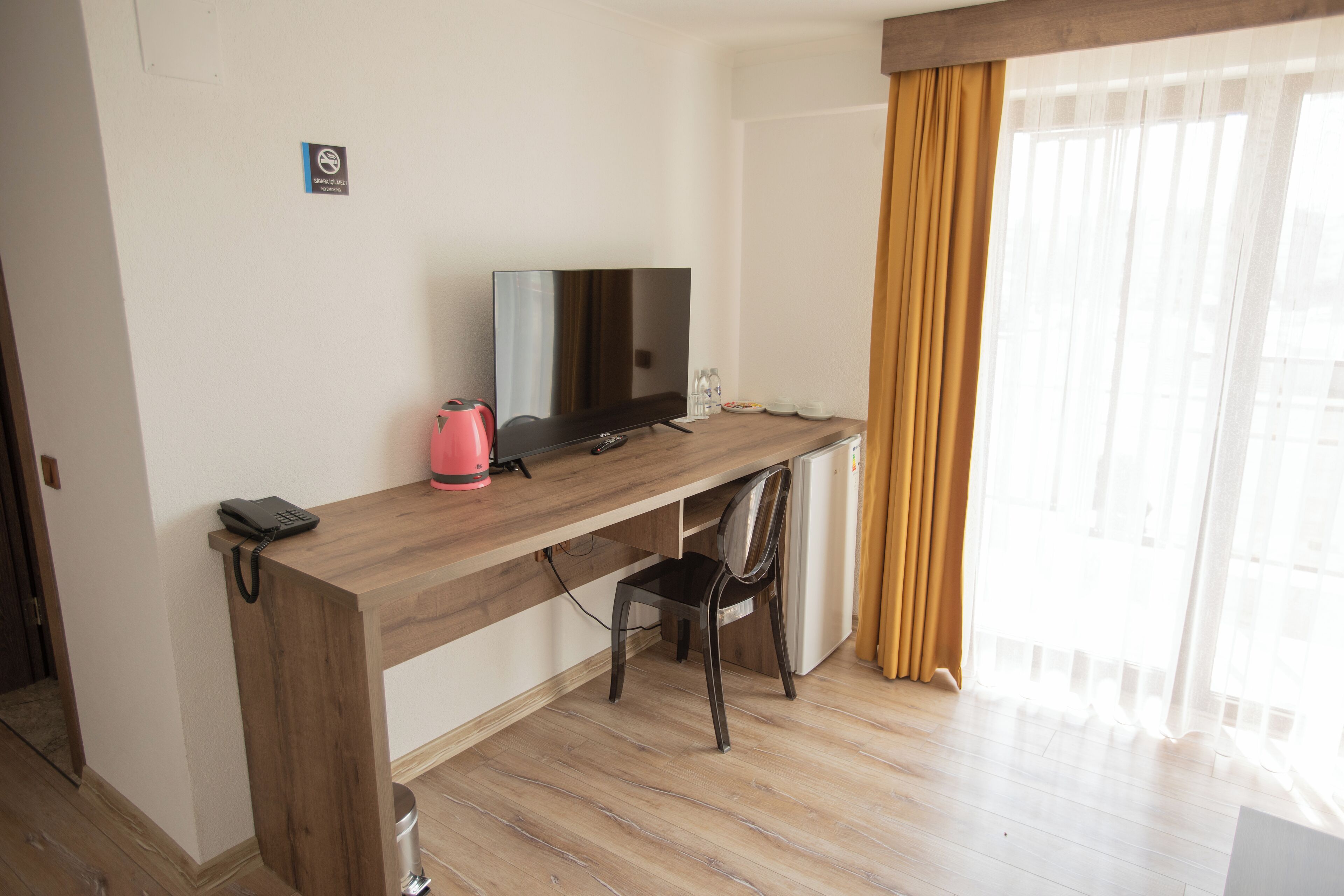 Quarto de hotel com escrivaninha de madeira, televisão, cadeira e lixeira.