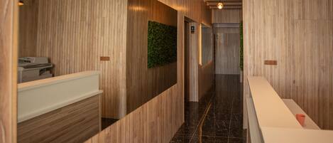 Un pasillo con paneles de madera, un mostrador de recepción y un elemento decorativo en una pared verde.