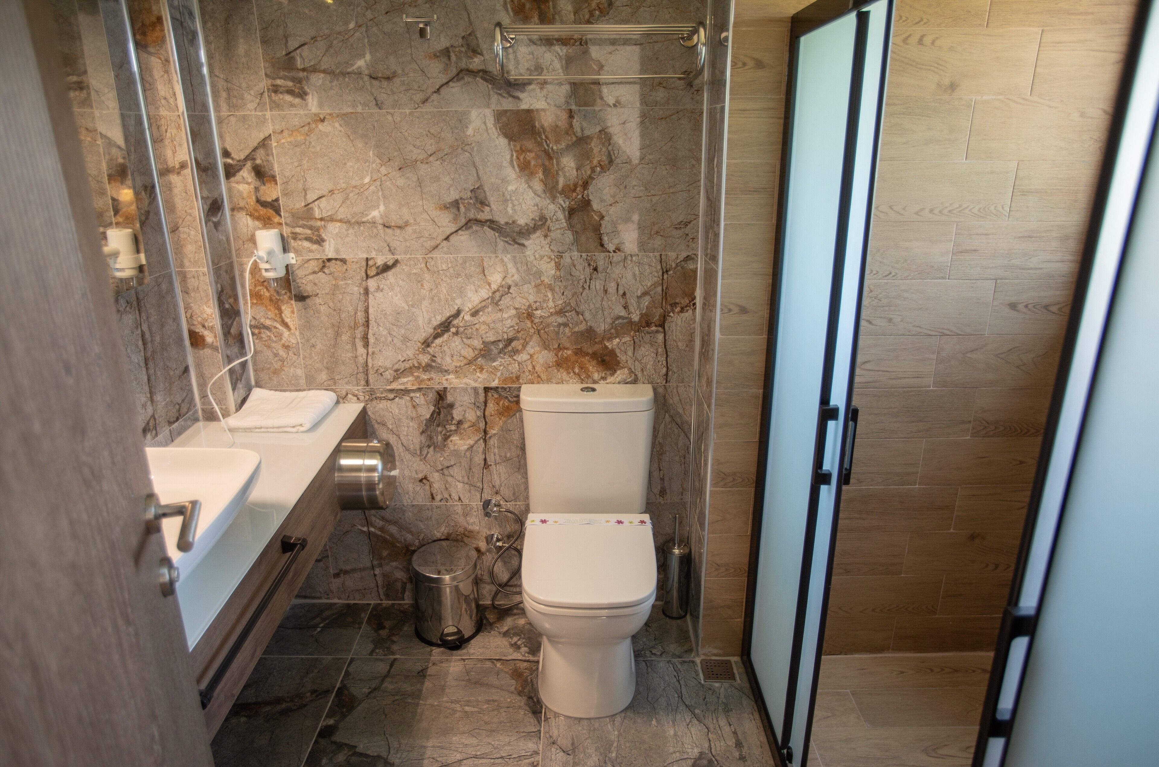 Un baño con pared de mármol, inodoro, lavabo y zona de ducha.