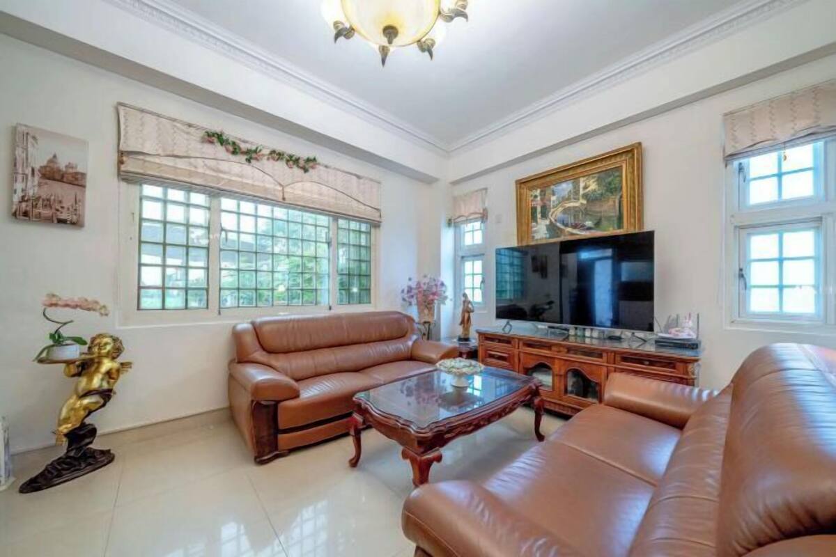 A spacious living room with leather sofas, a glass coffee table, a TV, and a fireplace.