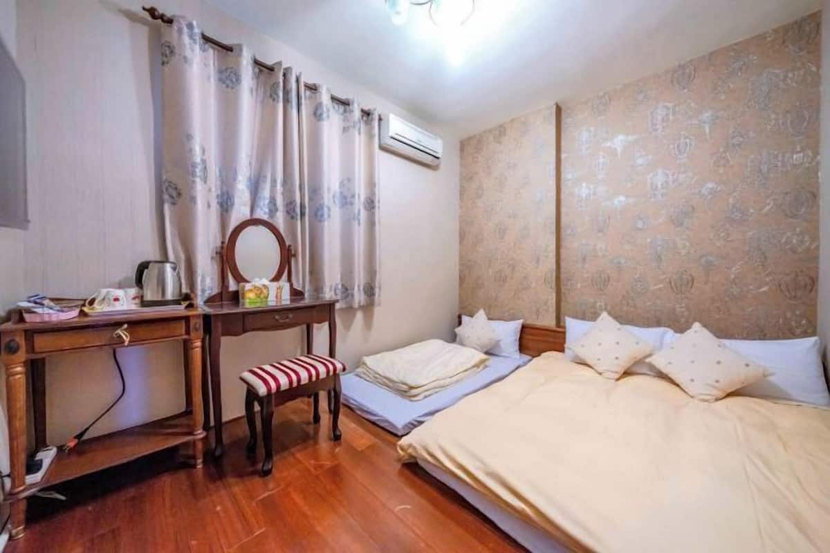 A room with a wooden desk, a chair, a bed with pillows, and a wall-mounted air conditioner.