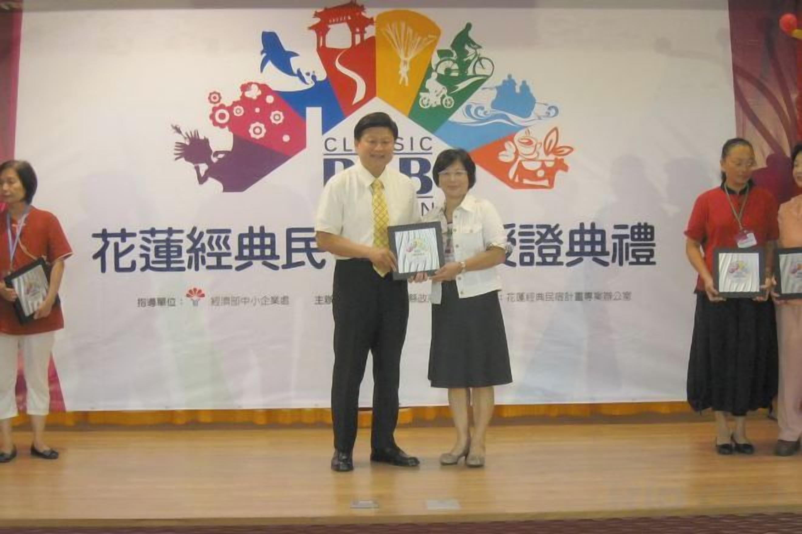 A stage with a banner featuring a logo and text, and people standing on it.