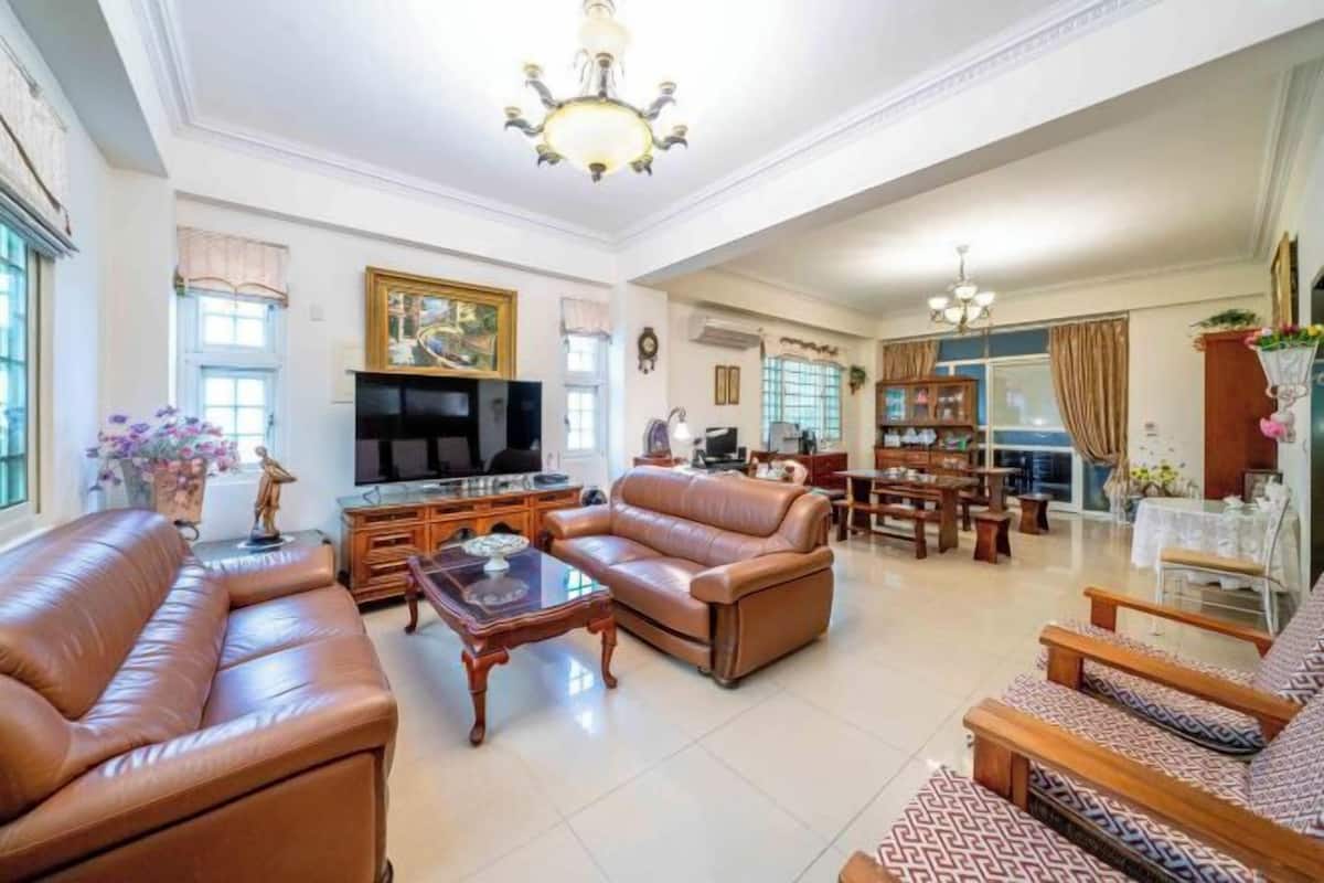 A spacious living room with leather sofas, a TV, and a dining area with wooden furniture.