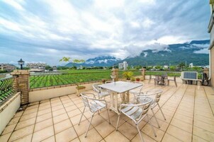 Un patio con mesa y sillas, vista a un campo verde y montañas al fondo.
