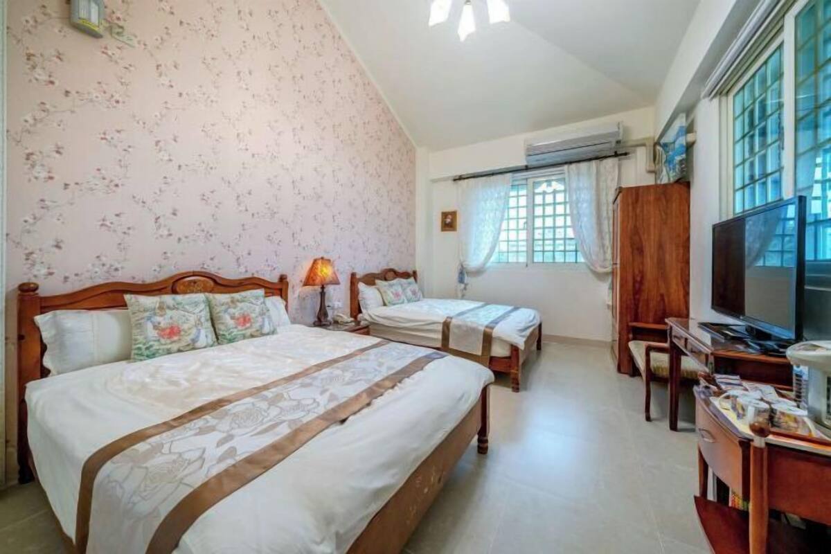 A bedroom with two beds, a TV, and a desk.