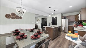 A modern kitchen with a dining area, featuring a wooden dining table set with red and black bowls, glasses, and cutlery. - "Final Frontier"- Pool, Hot Tub, Pickleball, Basketball, Pond, Arcade, Putt Putt (Troutman)