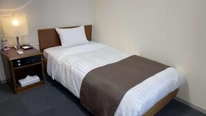 A hotel room with a single bed, a nightstand with a lamp, and a small shelf with a tissue box. - Shinjuku Urban Hotel (Tokyo)