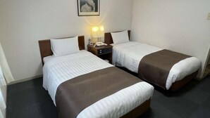 A hotel room with two beds, each with a brown headboard, white bedding, and a bedside table with a lamp. - Shinjuku Urban Hotel (Tokyo)